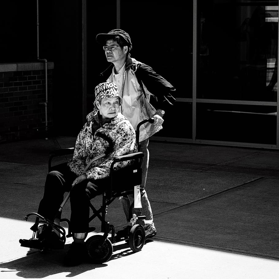 gray scale photo of man pushing wheelchair, grayscale photography of man assisting woman in wheelchair HD wallpaper
