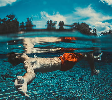 underwater photography of floating man wearing red shorts, man floating on body of water under white and blue sky HD wallpaper