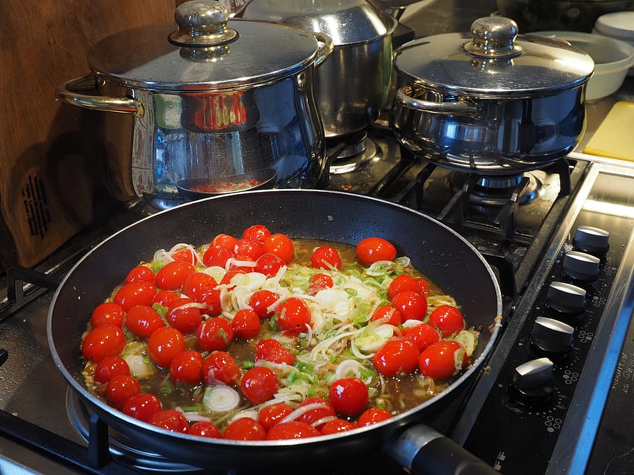 tomatoes and vegetables sauteed on black frying pan beside pots on gas range