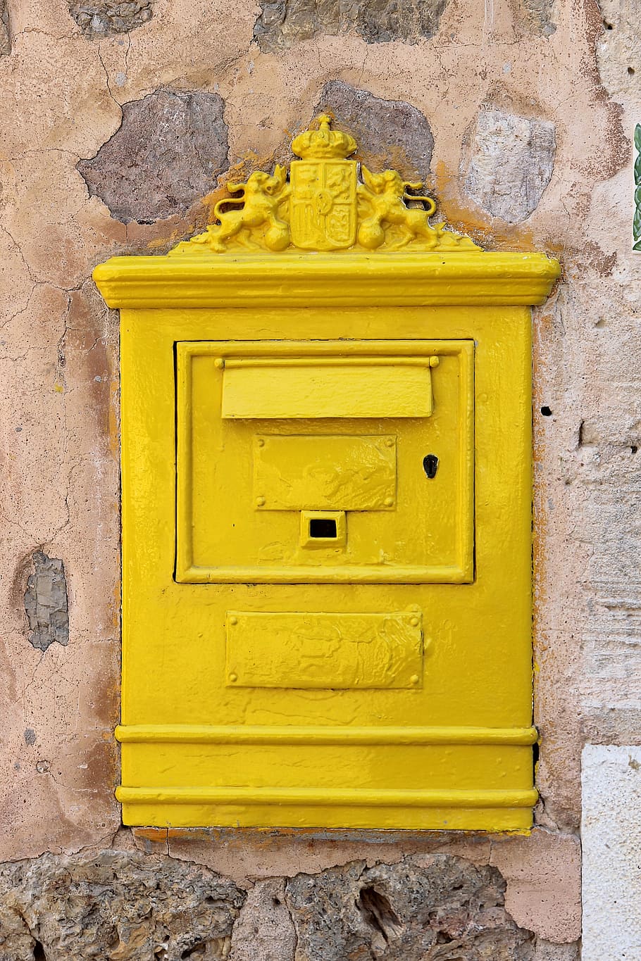 rectangular yellow metal box on brown concrete wall, mailbox