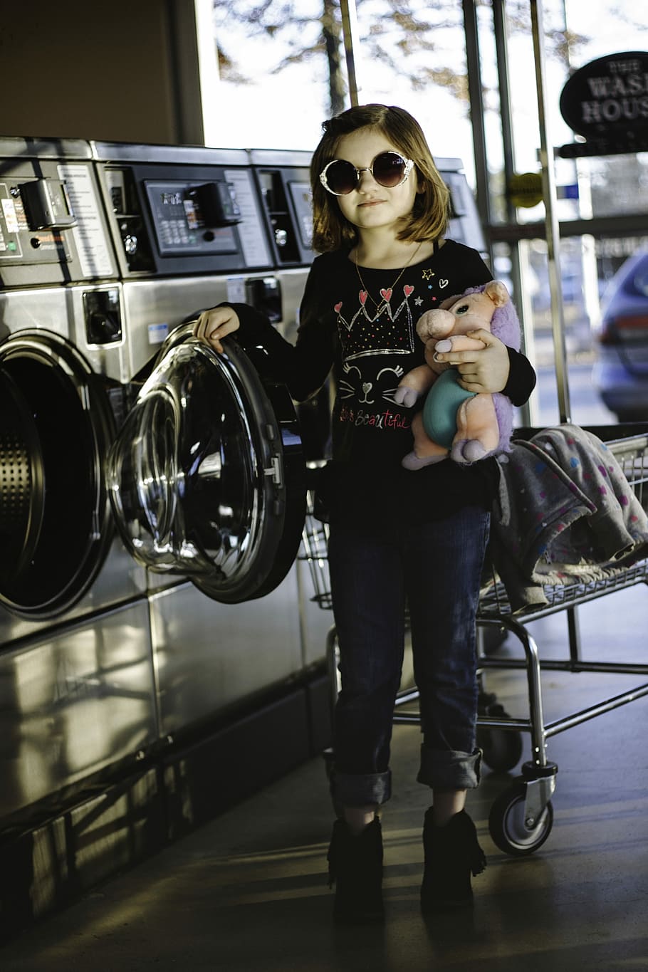 girl about to wash her plush toy, girl standing beside washing machine with her right hand on washing machine door
