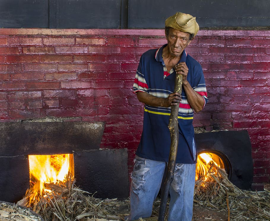 man wearing blue polo shirt near firepit, man stans holding stick near fireplace