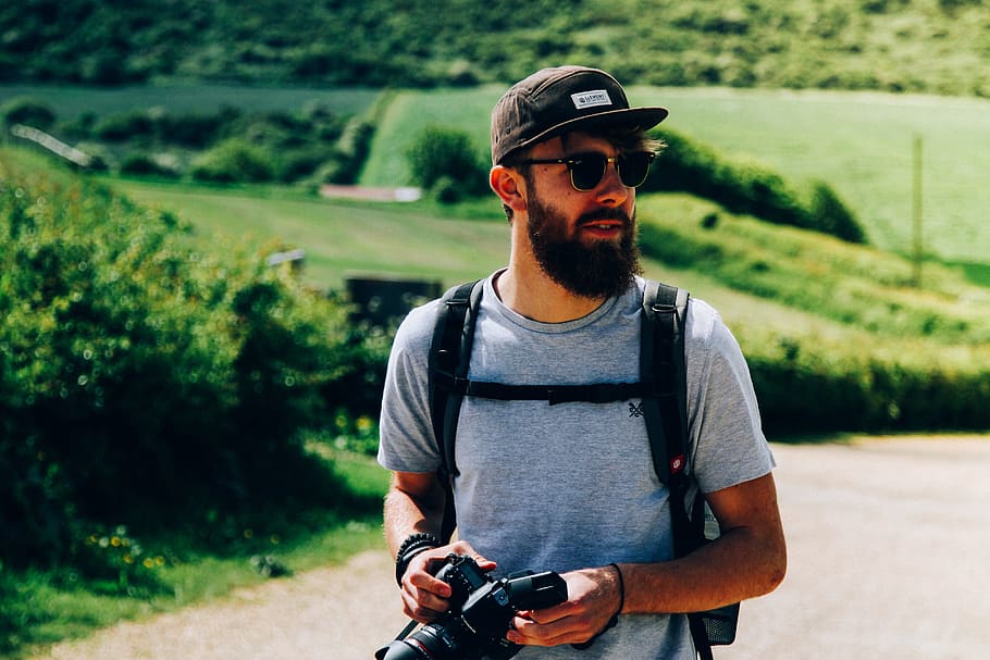 man wearing gray crew-neck t-shirt near grass field, man standing behind green field holding DSLR camera, HD wallpaper