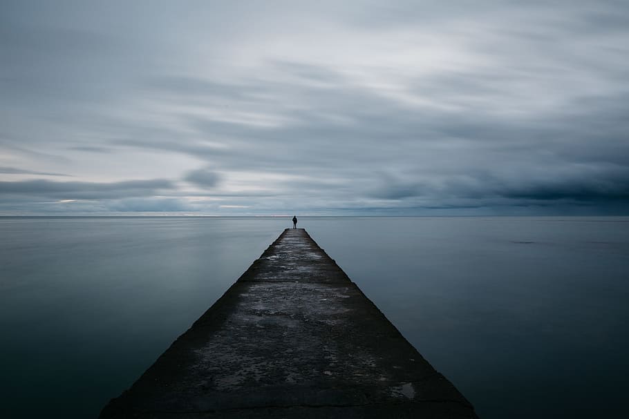 person standing on grey concrete pier under cloudy sky, person stand on ocean dock near body of water under cloudy sky HD wallpaper