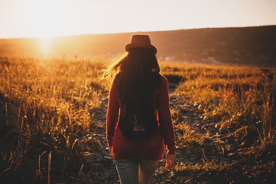 woman walking on grass plains during sunset, woman in red long-sleeved top waking in grass during golden hour