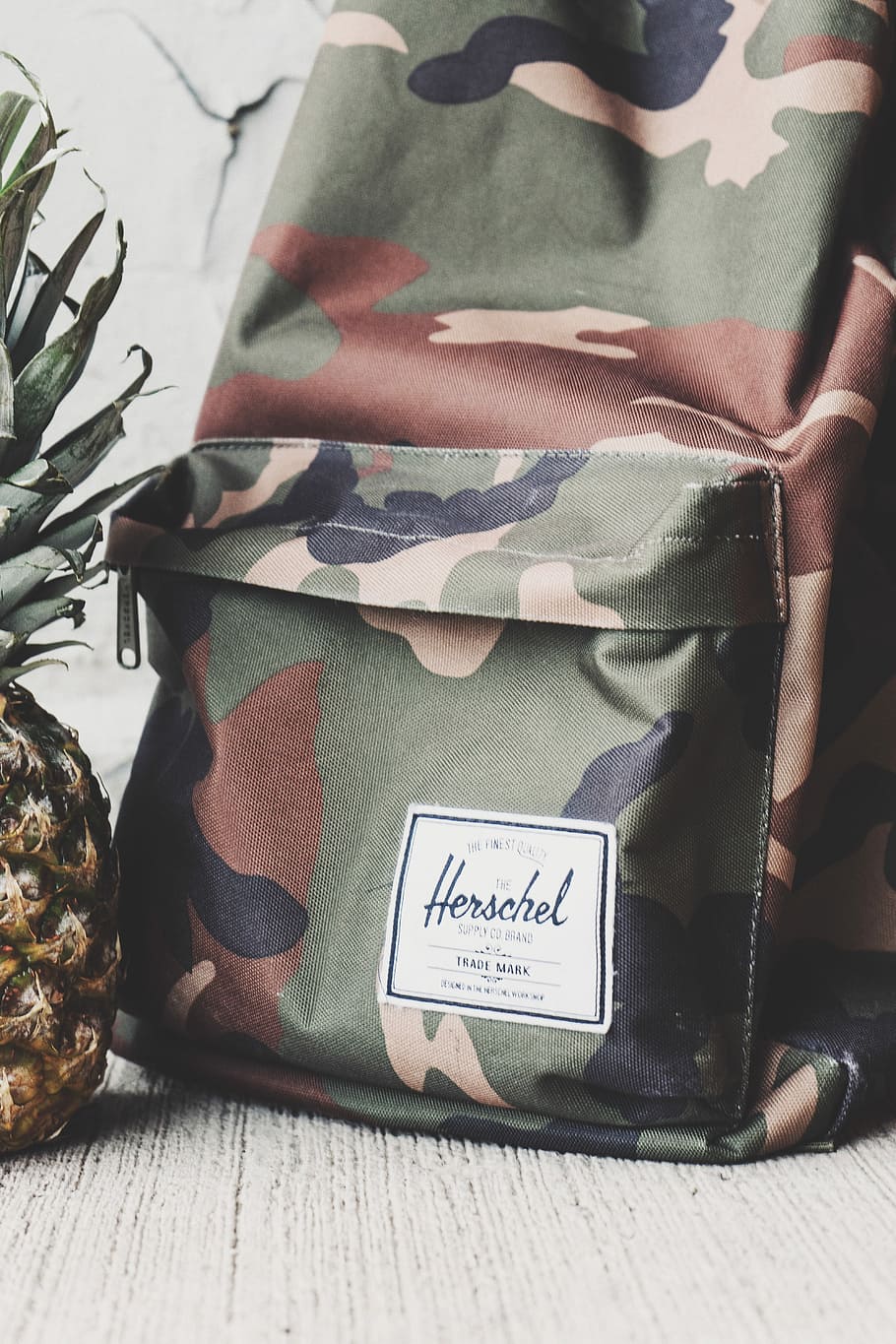 Cropped shot of a camo backpack and part of a pineapple., woodland camouflage Herschel backpack beside pineapple fruit HD wallpaper