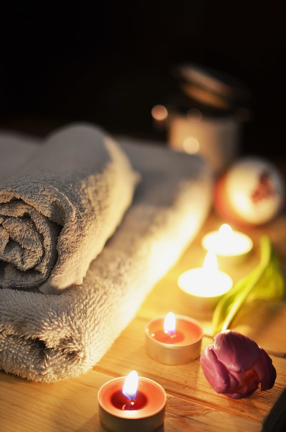 folded bath towel beside four lighted tealights on top of beige wooden table