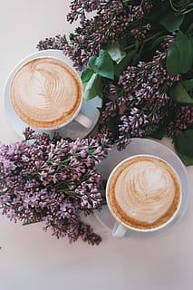 two white ceramic mugs filled with brown coffee placed on white ceramic saucers beside purple petaled flowers HD wallpaper