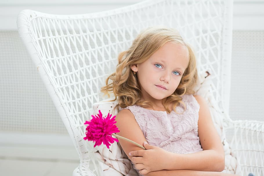 girl wearing pink floral top holding pink flower sitting on white chair