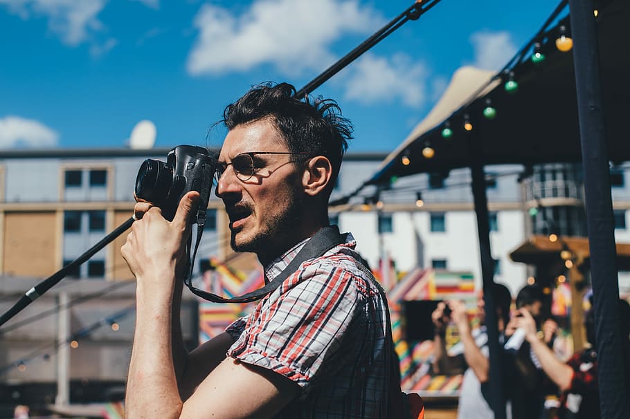 man taking a picture with DSLR camera, selective focus photo of man wearing eyeglasses taking a photo using black camera during daytime, HD wallpaper