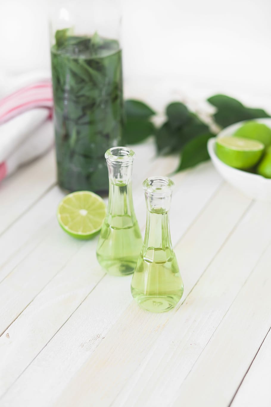 two clear glass bottles with lime juice on white wooden table, two filled clear glass bottles beside leaves and fruits HD wallpaper