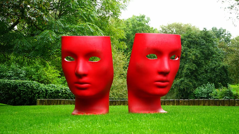 two red mask statue on green grass surrounded by trees, comedy tragedy masks