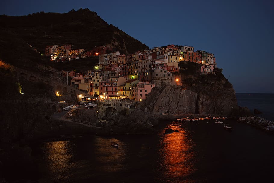 concrete houses on rocky hill beside large body of water during nighttime, buildings on cliff near body of water at night