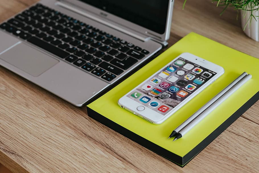Silver Acer laptop, a white Apple iPhone and a notepad on a wooden desk HD wallpaper