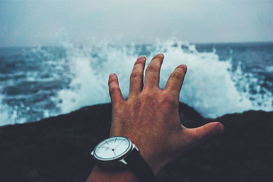 person wearing round white-face analog watch with splash of body of water in background HD wallpaper