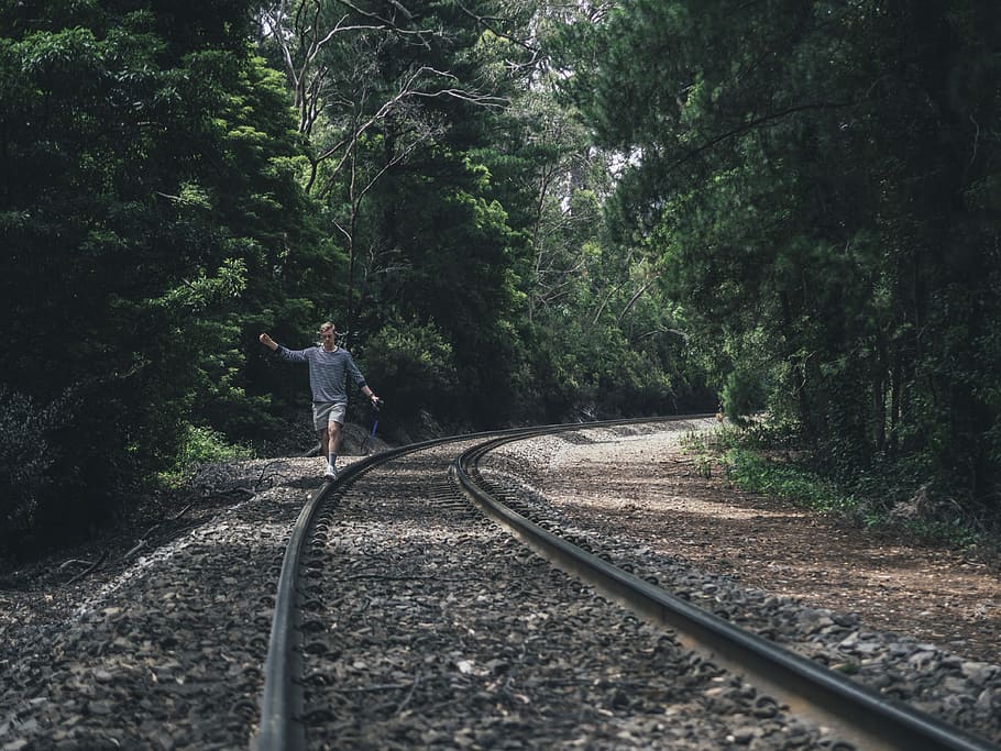 person walking through train rails between forest during daytime, man walking on side of train track HD wallpaper