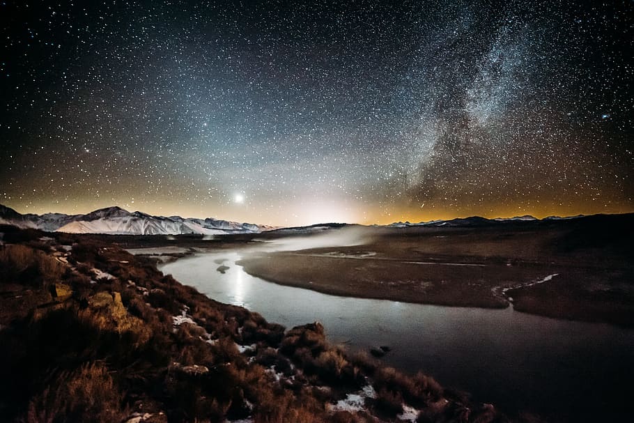river surrounded by brown grass field under star sky, landscape photo of river between barren field