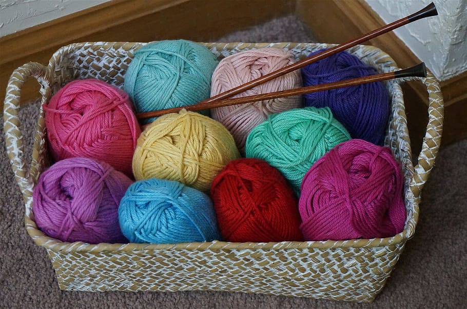 assorted-color yarn rolls in basket with hooks, wicker basket