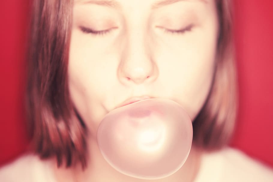 Chewing gum, selective focus photography of woman blowing gum