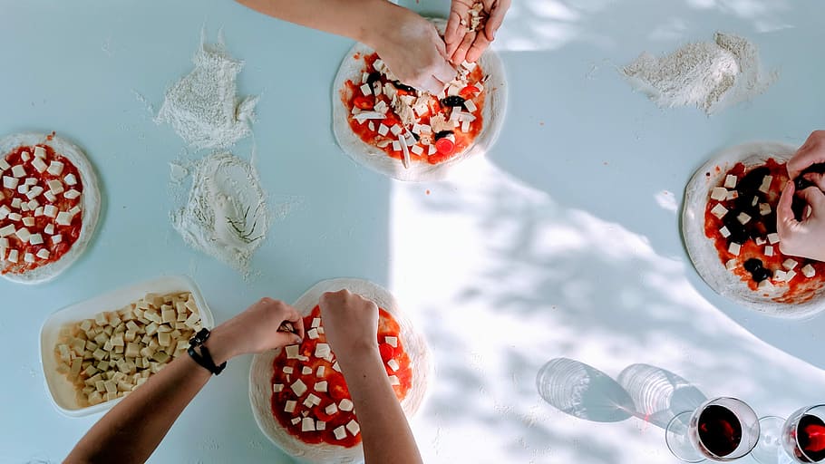 three person pouring cheeses on pizza doughs during daytime HD wallpaper