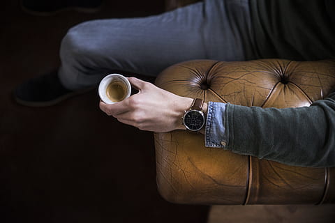 person sitting on brown leather couch holding coffee cup, man HD wallpaper