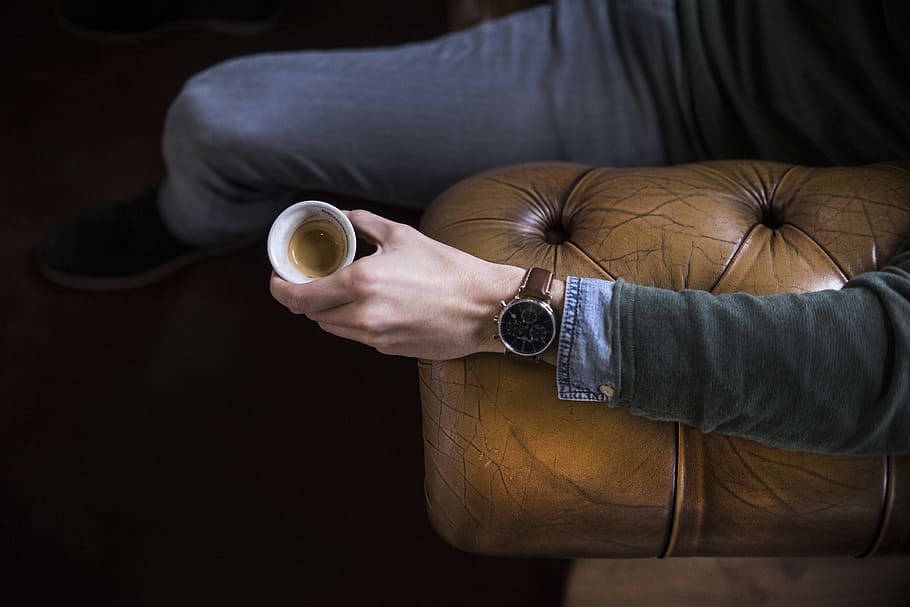 person sitting on brown leather couch holding coffee cup, man HD wallpaper