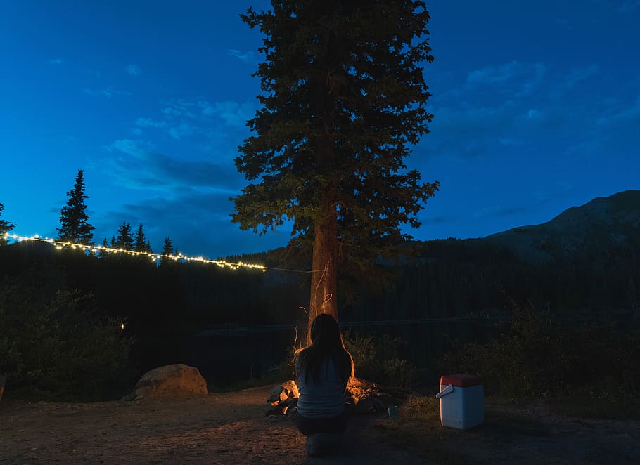 woman sitting in front of tree, woman sitting beside fire, camping