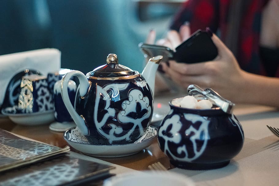 person sitting in front white and black ceramic tea set, white and black ceramic teapot on table