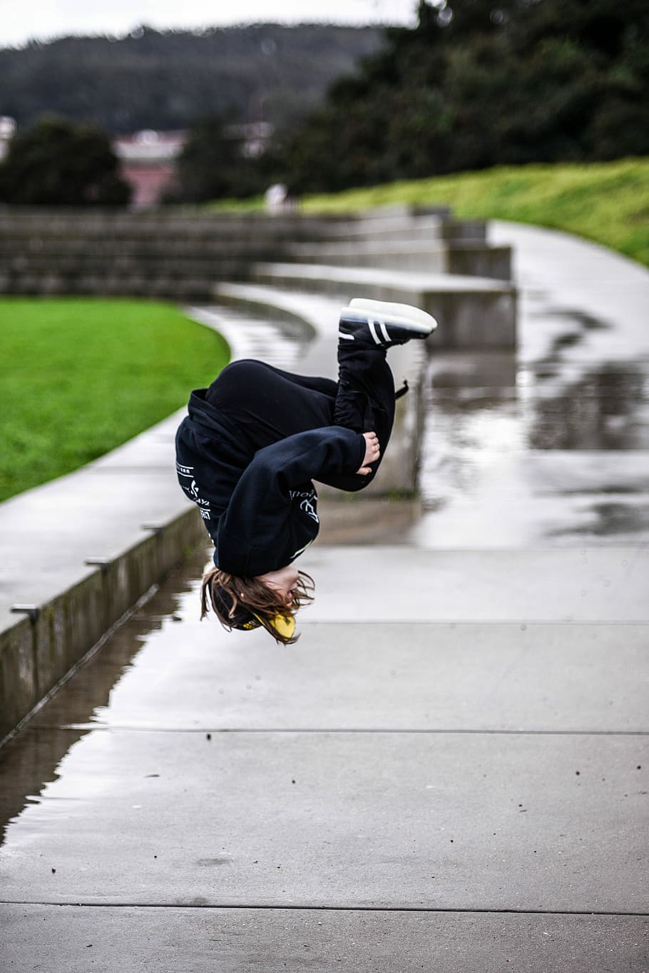person wears black jacket and black pants doing flip on gray concrete walkway with water during daytime selective focus photography, black pants, HD wallpaper