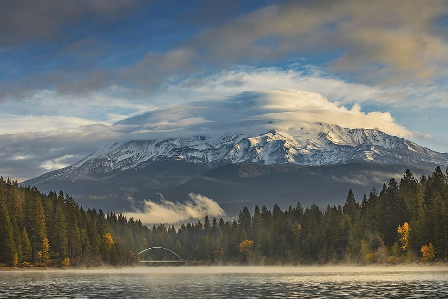 snow covered mountain surrounded by pine trees, body of water beside green trees HD wallpaper