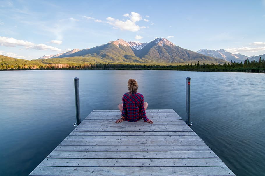 woman sitting on dock bridge near lake during daytime, woman sitting on dock near lake in a distance of mountains HD wallpaper
