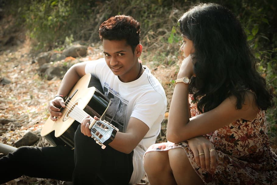man in white shirt sitting playing guitar with woman beside, romantic
