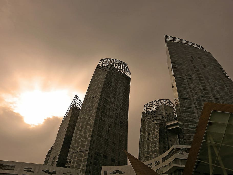 low-angle photography of high-rise buildings under sun shining through grey clouds HD wallpaper