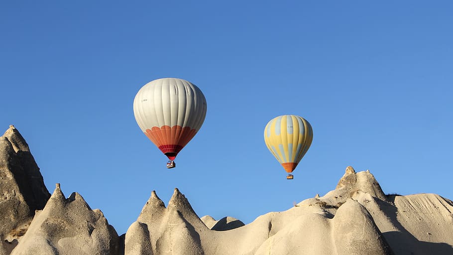 two white and gray air balloons under hills at dayatime, cappadocia
