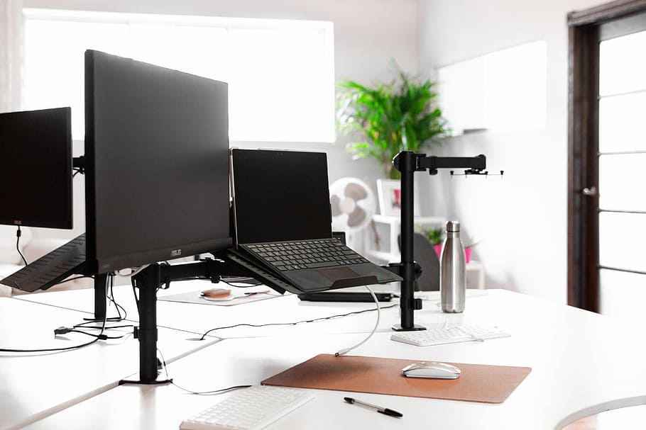 laptop, monitor, and vacuum flask on white table, desk with laptop and monitor turned off