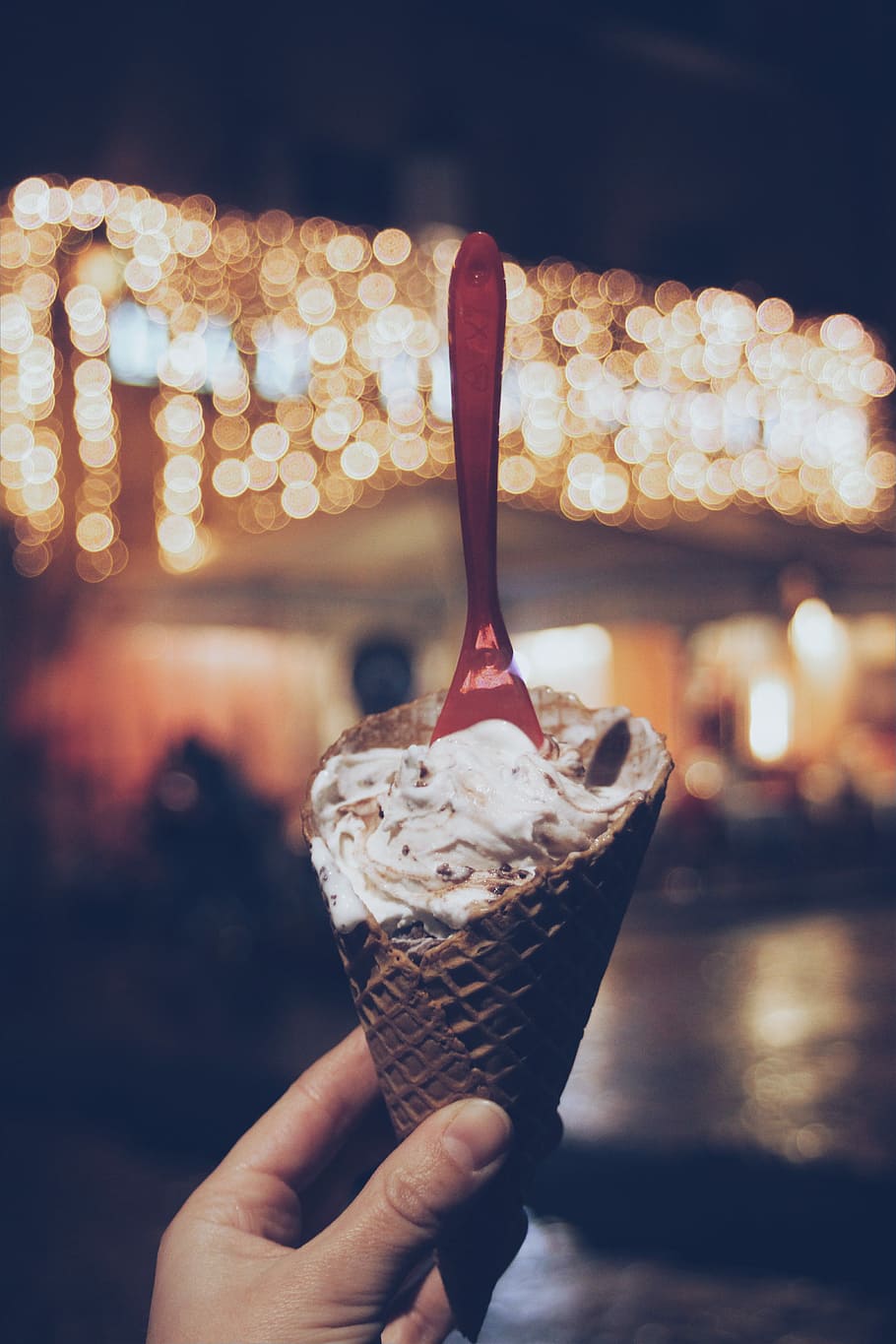 person holding sugar cone with white cream and plastic spoon, bokeh photography of person holding ice cream cone