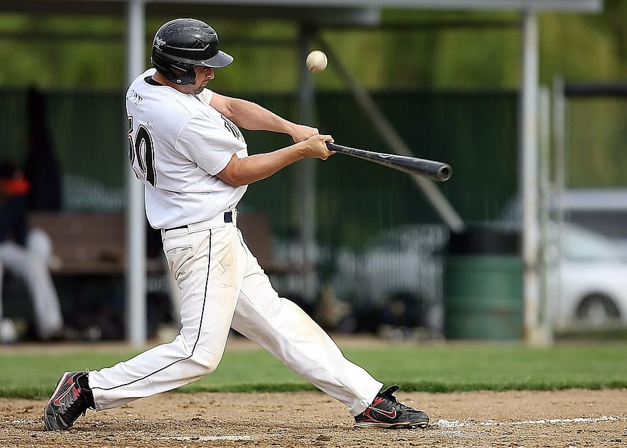 baseball player swinging baseball bat over white baseball, batter