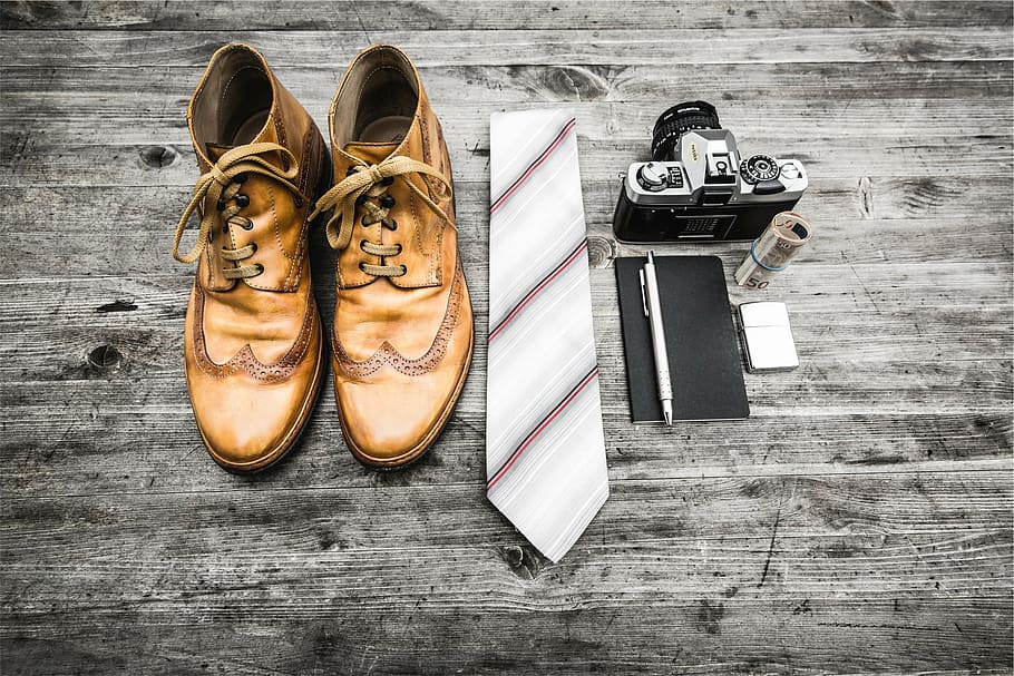 pair of brown leather shoes beside white and brown striped necktie and gray SLR camera