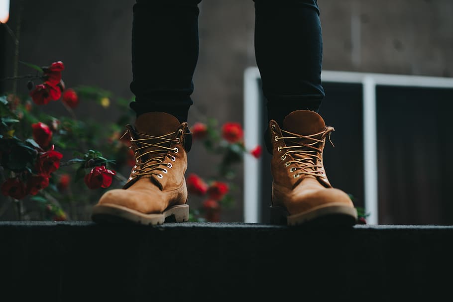 person wearing brown boots standing near red flowers, person standing on concrete surface HD wallpaper