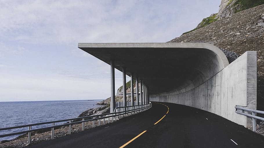 white road tunnel beside sea, empty road near body of water, building HD wallpaper