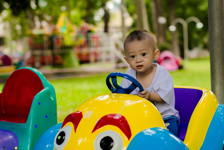 child rides yellow and purple car toy, play, park, kid, ku shin