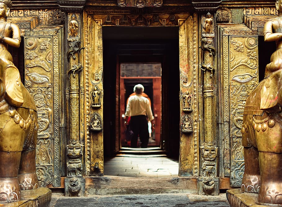 man standing in front of brown doorway during daytime, man standing near brass-colored concrete building HD wallpaper
