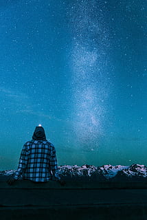 man sitting on gray wall looking at the stars, person in blue and black plaid sports shirt watching milkyway HD wallpaper