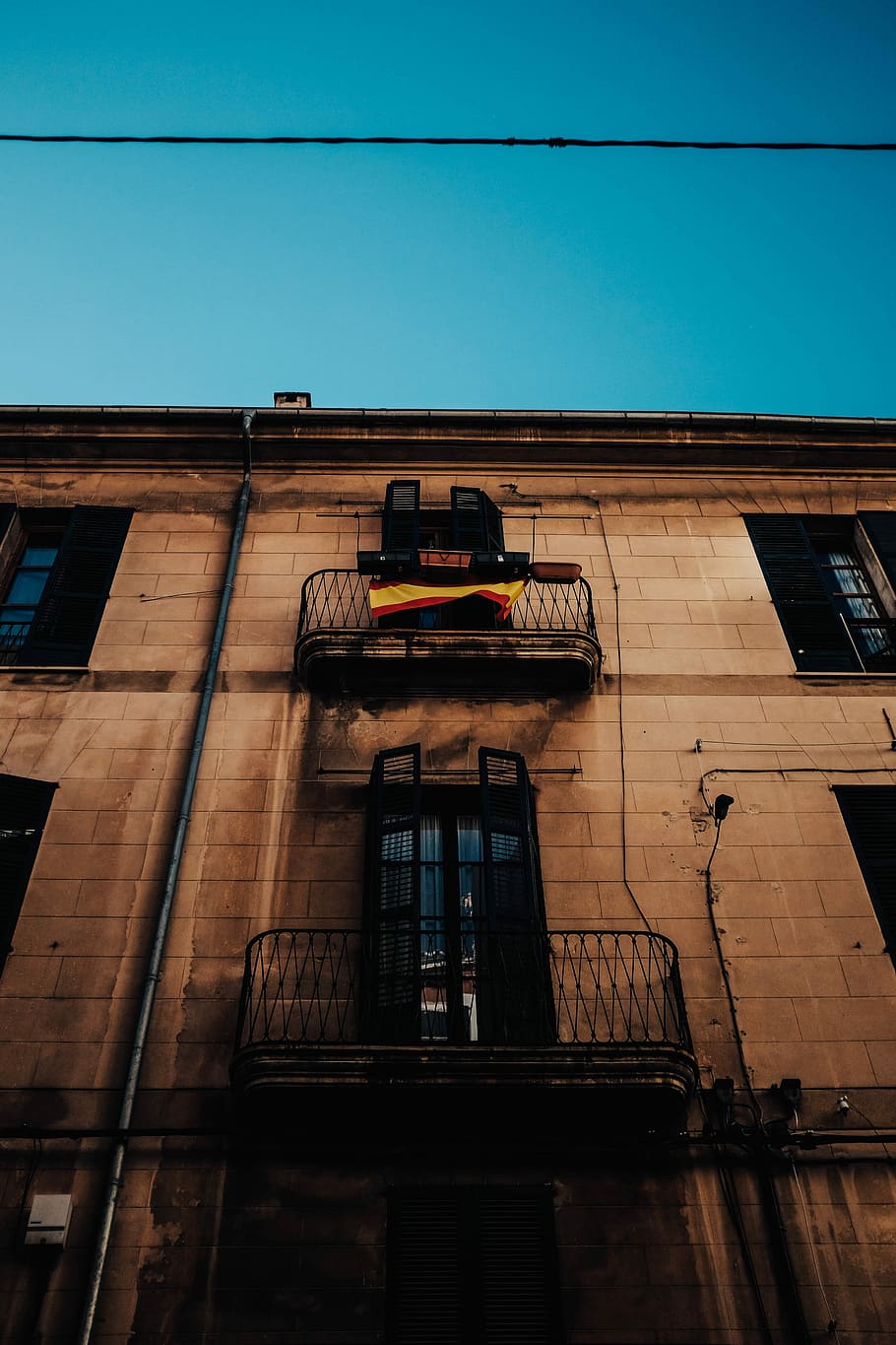 low angle photography showing building's windows, black, red, and yellow striped flag on metal terrace HD wallpaper