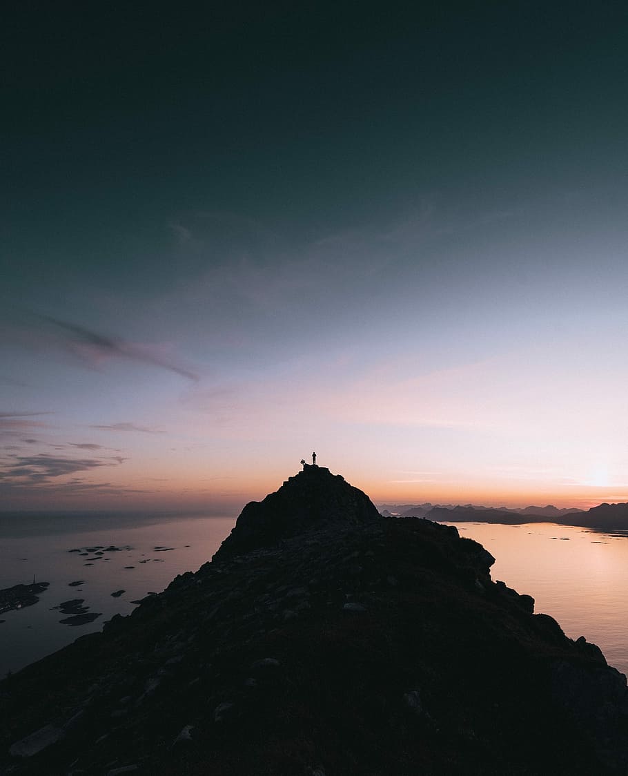 silhouette on person standing on top mountain cliff, silhouette photography of rock formation near body of water HD wallpaper