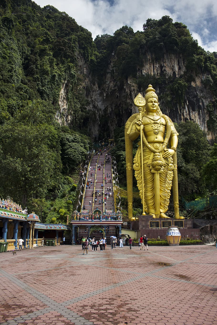 group of people walking beside gold Hindu god statue, batu, caves