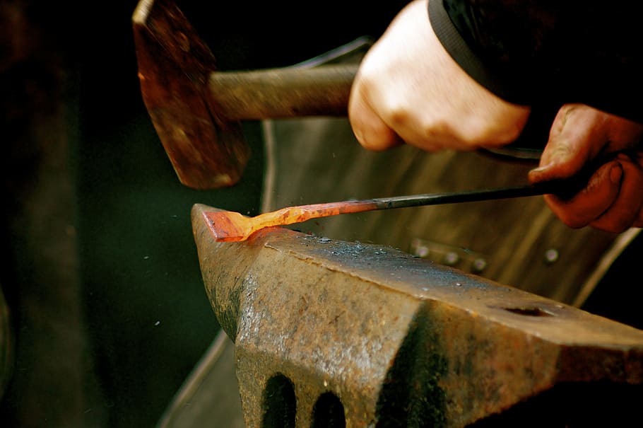 person welding a metal with hammer on anvil, fire, iron, forge