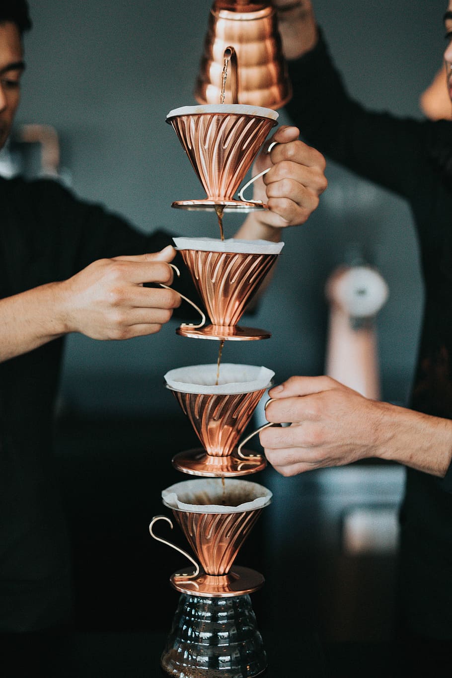 two person pouring coffee with piled cups, two men holding brass-colored mugs while pouring tea HD wallpaper
