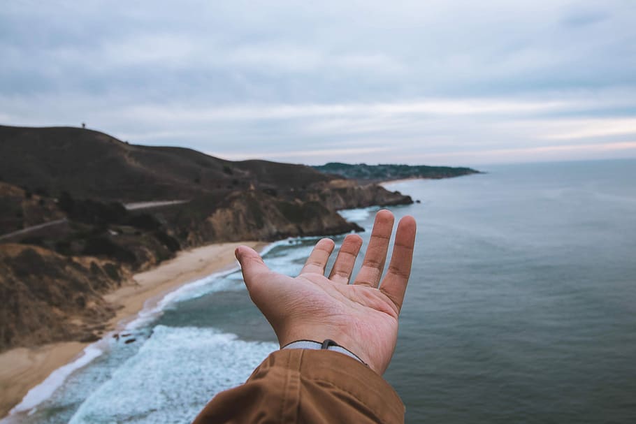 person hand front of sea and cliff, person left hand near body of water HD wallpaper