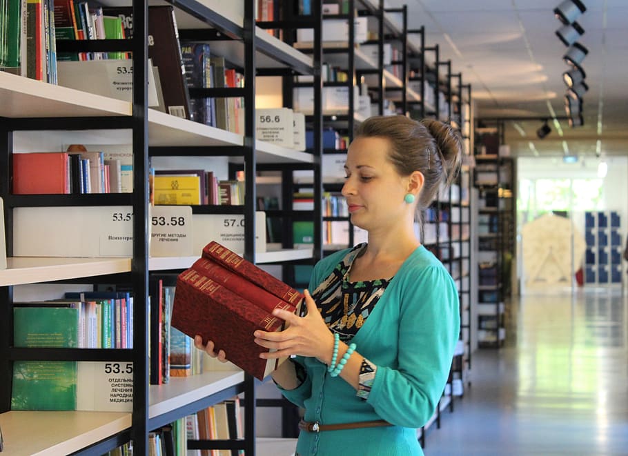 woman wearing teal top holding books, girl, shelves, library